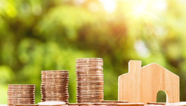 A stack of coins next to the model of a small wooden house indicating how staging help increase the value of a house