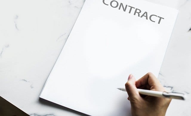 A hand holding a pen about to sign an agreement for the sale of a property to an home investor