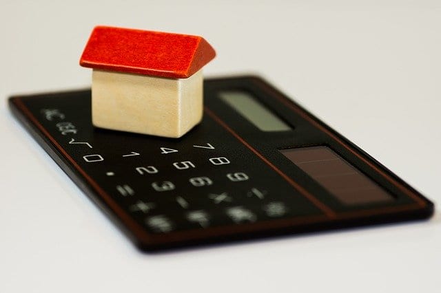 A miniture home on a small calculate that is used to calculate a home investment transaction details